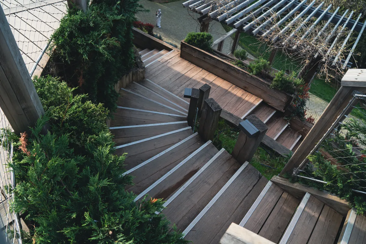Wooden staircase leading down a tiered deck surrounded by greenery, Millard